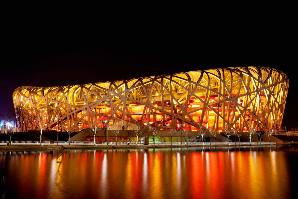 Modern stadium with a unique architectural design illuminated at night, reflected in water.